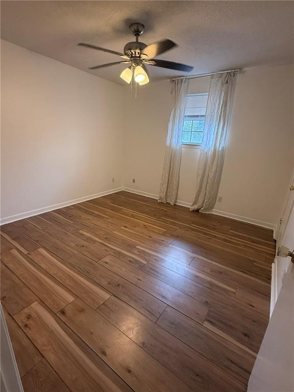 unfurnished room with wood-type flooring, a textured ceiling, and baseboards