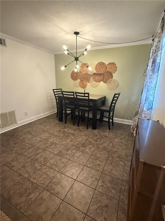 dining space with a chandelier, a textured ceiling, visible vents, baseboards, and crown molding