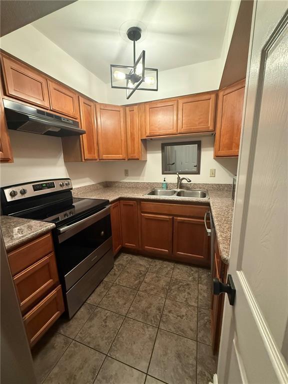 kitchen with under cabinet range hood, dark tile patterned floors, a sink, brown cabinets, and stainless steel electric range oven