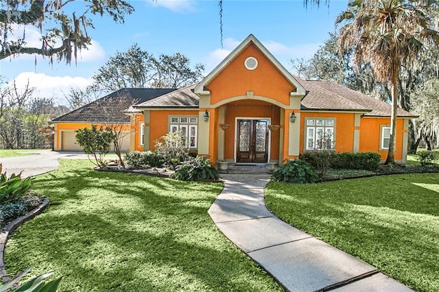 view of front of house featuring french doors, stucco siding, an attached garage, a front yard, and driveway