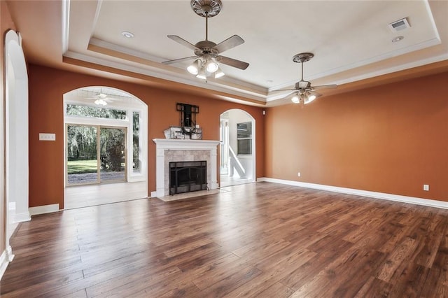 unfurnished living room featuring arched walkways, wood finished floors, a raised ceiling, and a ceiling fan