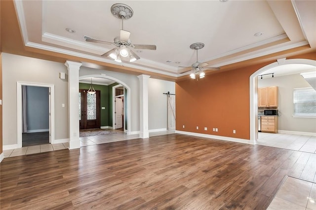 unfurnished living room featuring arched walkways, a tray ceiling, a ceiling fan, and light wood-style floors