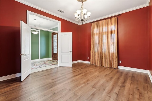 empty room with baseboards, visible vents, ornamental molding, wood finished floors, and a notable chandelier