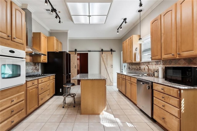 kitchen with a barn door, wall chimney range hood, a center island, black appliances, and a sink