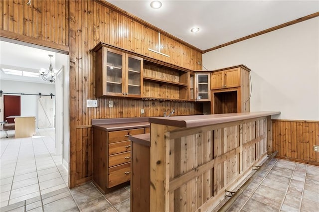 bar featuring a barn door, wood walls, ornamental molding, wainscoting, and an inviting chandelier