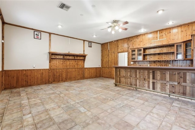 kitchen with wooden walls, visible vents, a ceiling fan, wainscoting, and glass insert cabinets