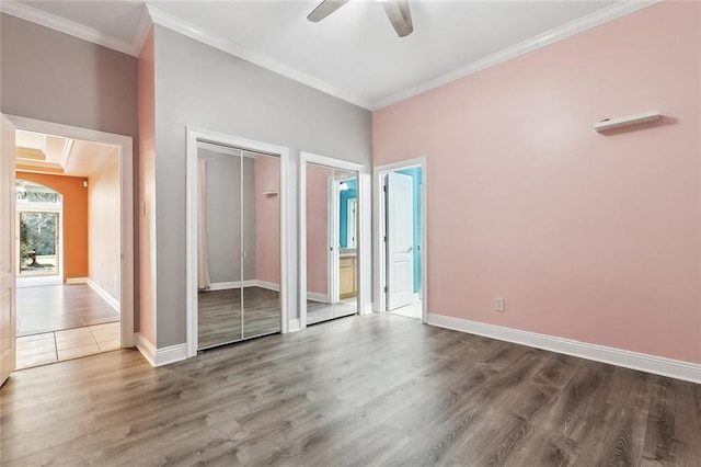 unfurnished bedroom featuring wood finished floors, crown molding, baseboards, and two closets