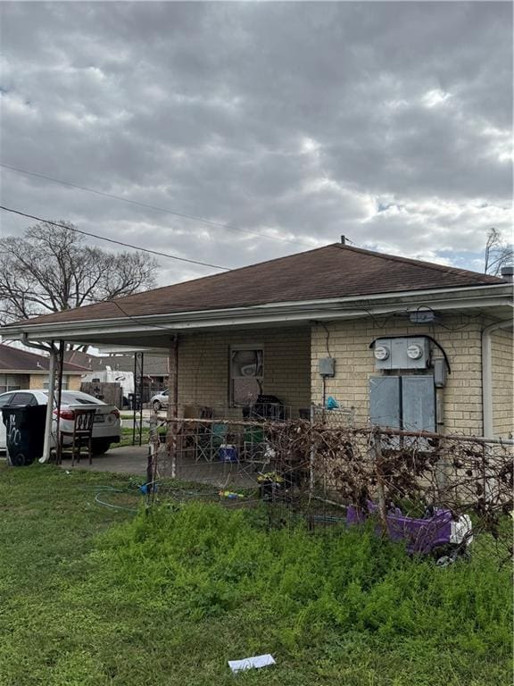 rear view of property with an attached carport, brick siding, a lawn, and roof with shingles