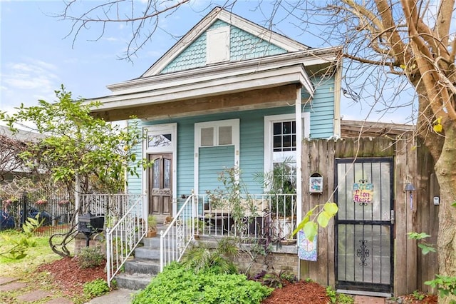 shotgun-style home featuring covered porch and fence