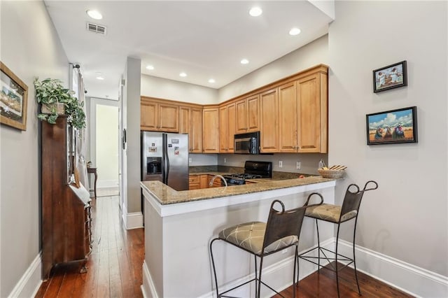 kitchen with stone counters, a peninsula, dark wood-type flooring, visible vents, and appliances with stainless steel finishes