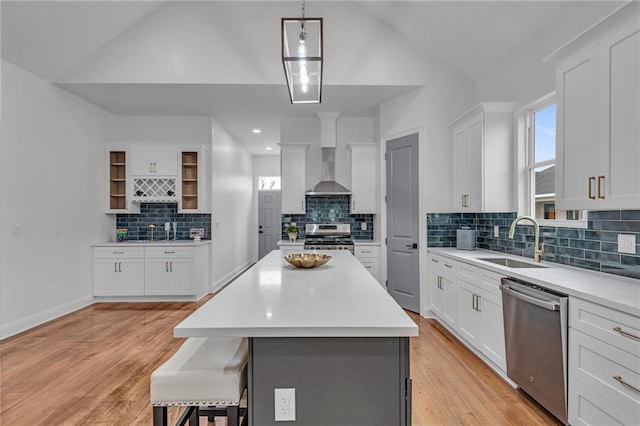 kitchen featuring wall chimney exhaust hood, light wood-style flooring, stainless steel appliances, a kitchen bar, and a sink