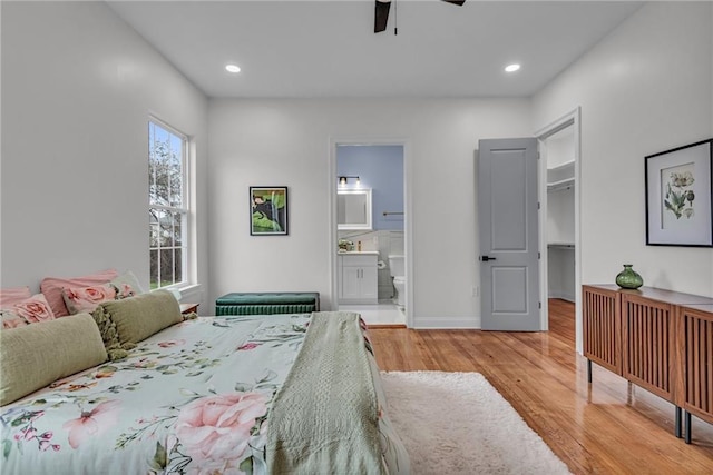 bedroom featuring baseboards, ensuite bathroom, a spacious closet, light wood-style floors, and recessed lighting