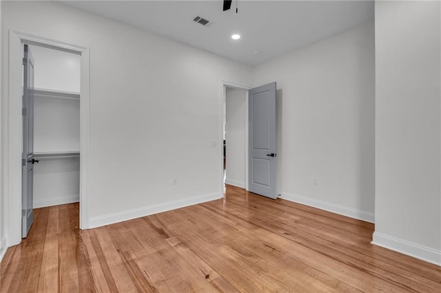 unfurnished bedroom with light wood-style flooring, visible vents, a walk in closet, and baseboards