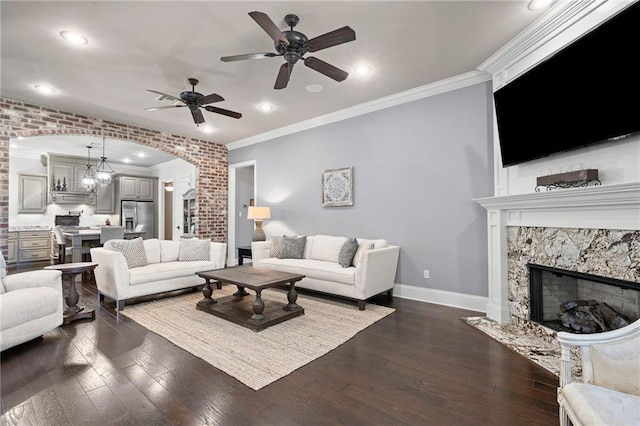 living area featuring baseboards, arched walkways, dark wood finished floors, crown molding, and a fireplace