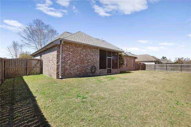 rear view of property with a shingled roof, brick siding, a lawn, and a fenced backyard