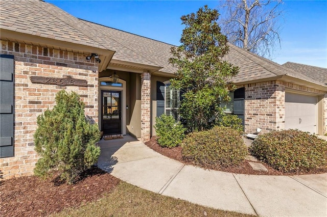 property entrance with brick siding, an attached garage, and a shingled roof