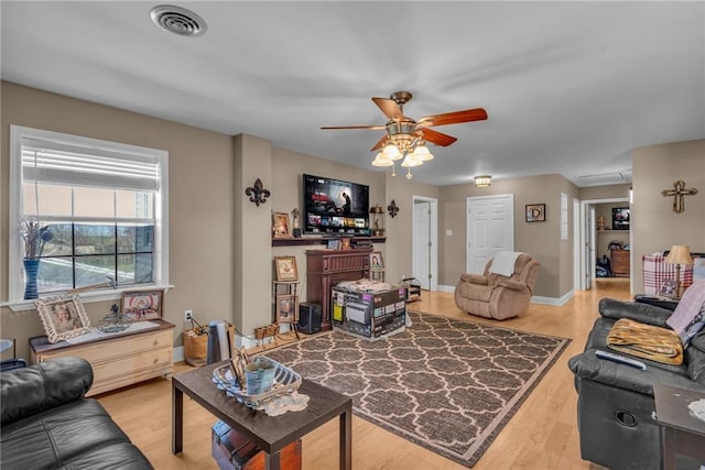 living area featuring light wood-style floors, visible vents, baseboards, and a ceiling fan