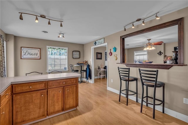 kitchen with visible vents, brown cabinetry, a kitchen breakfast bar, light countertops, and light wood-type flooring