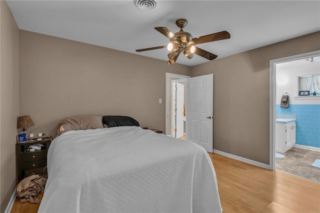 bedroom featuring tile walls, light wood finished floors, visible vents, ensuite bathroom, and ceiling fan