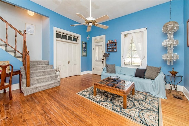 living room with stairs, visible vents, wood finished floors, baseboards, and ceiling fan with notable chandelier