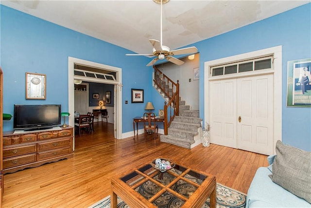 living room with a ceiling fan, stairway, baseboards, and wood finished floors