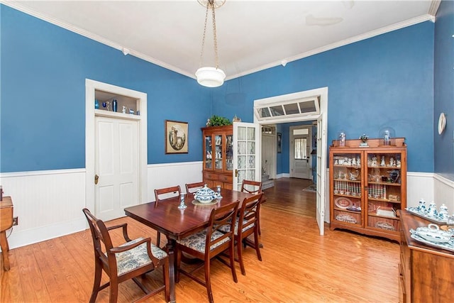 dining area with a wainscoted wall, light wood-style flooring, and crown molding