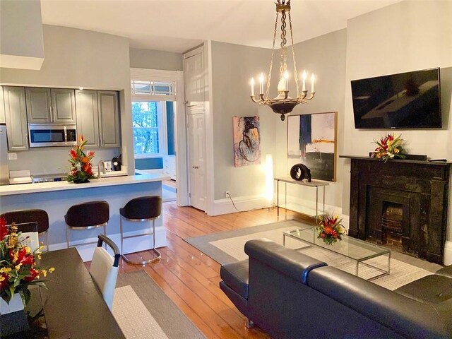 living room featuring light wood finished floors, a fireplace with flush hearth, baseboards, and a notable chandelier