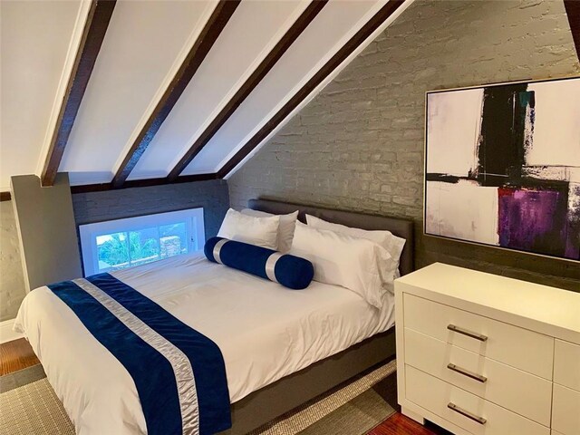 bedroom with brick wall, vaulted ceiling, and wood finished floors