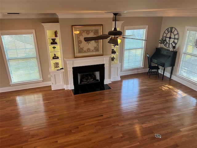 unfurnished living room featuring wood finished floors, ceiling fan, ornamental molding, and a fireplace with flush hearth