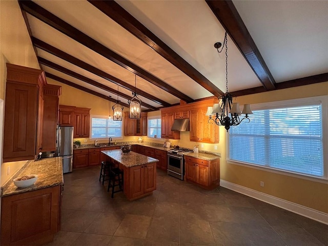 kitchen featuring baseboards, appliances with stainless steel finishes, a center island, under cabinet range hood, and a notable chandelier