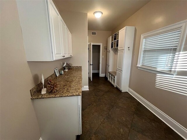 kitchen featuring baseboards, visible vents, light stone countertops, and white cabinets