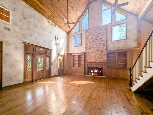 unfurnished living room featuring hardwood / wood-style flooring, a lit fireplace, visible vents, and ceiling fan