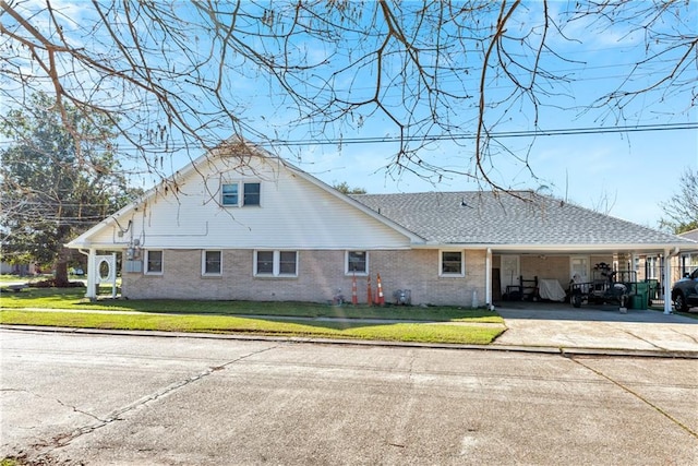 back of house with a shingled roof, concrete driveway, a carport, a lawn, and brick siding