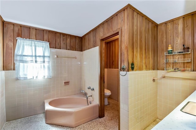 bathroom with wood walls, toilet, wainscoting, tile walls, and a sink