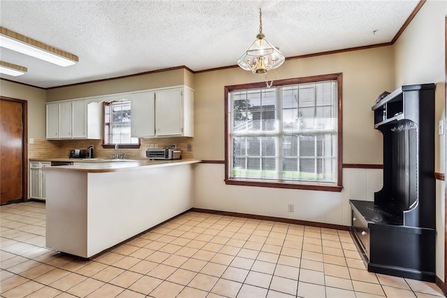 kitchen with light tile patterned floors, hanging light fixtures, ornamental molding, white cabinets, and a peninsula