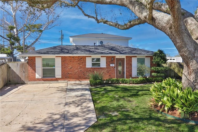 view of front facade with brick siding, a front lawn, a shingled roof, and fence