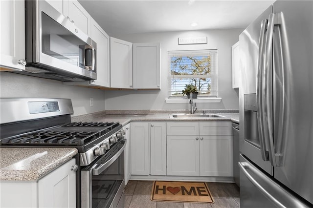 kitchen with wood finished floors, appliances with stainless steel finishes, a sink, and white cabinets