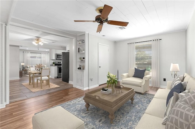 living room featuring wood finished floors, a ceiling fan, visible vents, baseboards, and crown molding