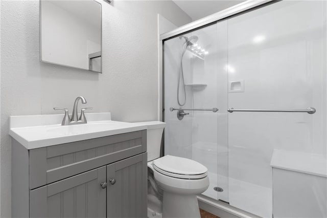 full bath with toilet, a textured wall, a shower stall, and vanity