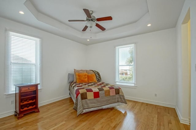 bedroom with light wood-style flooring, baseboards, a raised ceiling, and recessed lighting