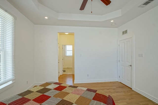 unfurnished bedroom featuring a tray ceiling, light wood-type flooring, visible vents, and recessed lighting