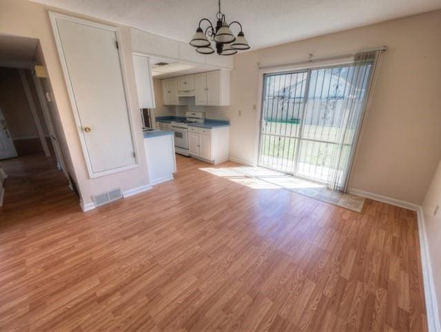 unfurnished dining area with a notable chandelier, light wood finished floors, visible vents, and baseboards