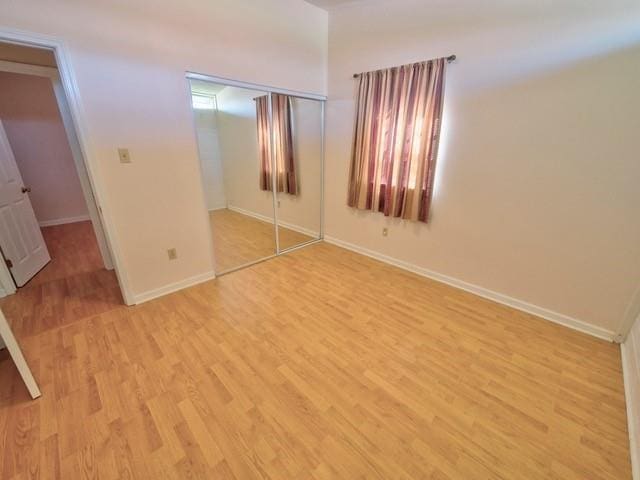 unfurnished bedroom featuring light wood finished floors, baseboards, and a closet