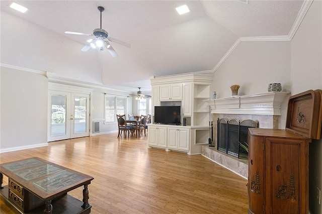 living room featuring light wood finished floors, a tiled fireplace, ceiling fan, crown molding, and french doors