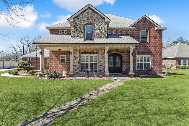 view of front of house with covered porch, brick siding, french doors, roof with shingles, and a front yard