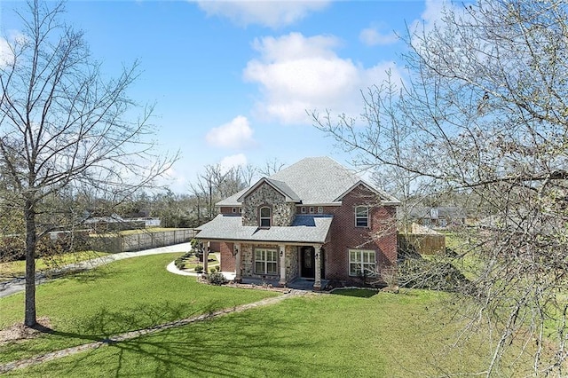 back of house featuring brick siding, stone siding, fence, and a yard