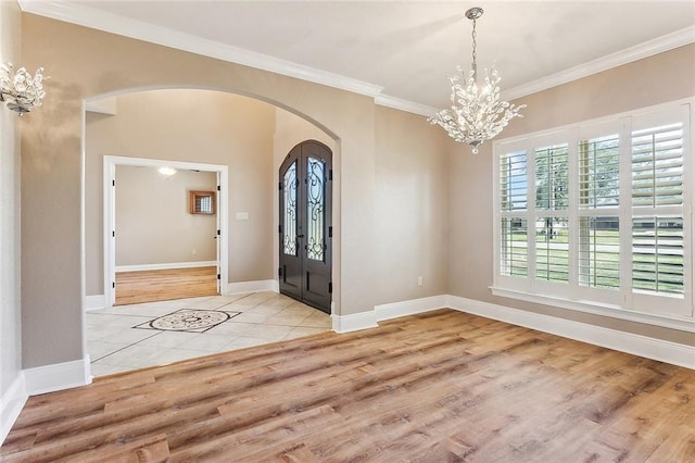 foyer featuring arched walkways, crown molding, baseboards, and wood finished floors