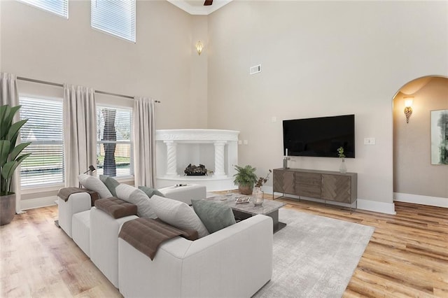 living area with baseboards, visible vents, arched walkways, wood finished floors, and a high ceiling