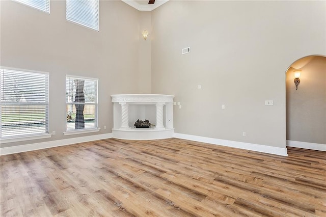 unfurnished living room featuring arched walkways, a fireplace with raised hearth, wood finished floors, visible vents, and baseboards