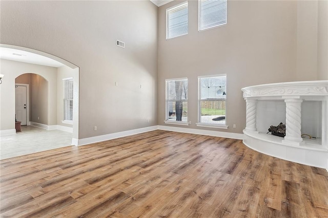 unfurnished living room with arched walkways, a tile fireplace, light wood-style flooring, and baseboards